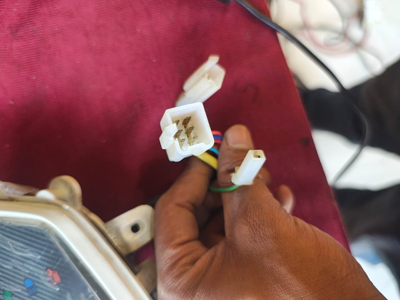 Hand holding a small electrical connector against a red fabric background