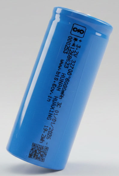 Blue cylindrical battery on a red surface with electronic devices in the background